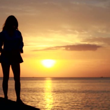 happy woman, pondering life, overlooking the water at sunset
