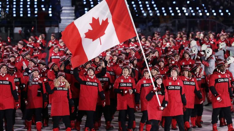 Team Canada athletes smile while holding Canadian Flag