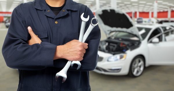 A mechanic with his tools infront of a white car with its hood open.