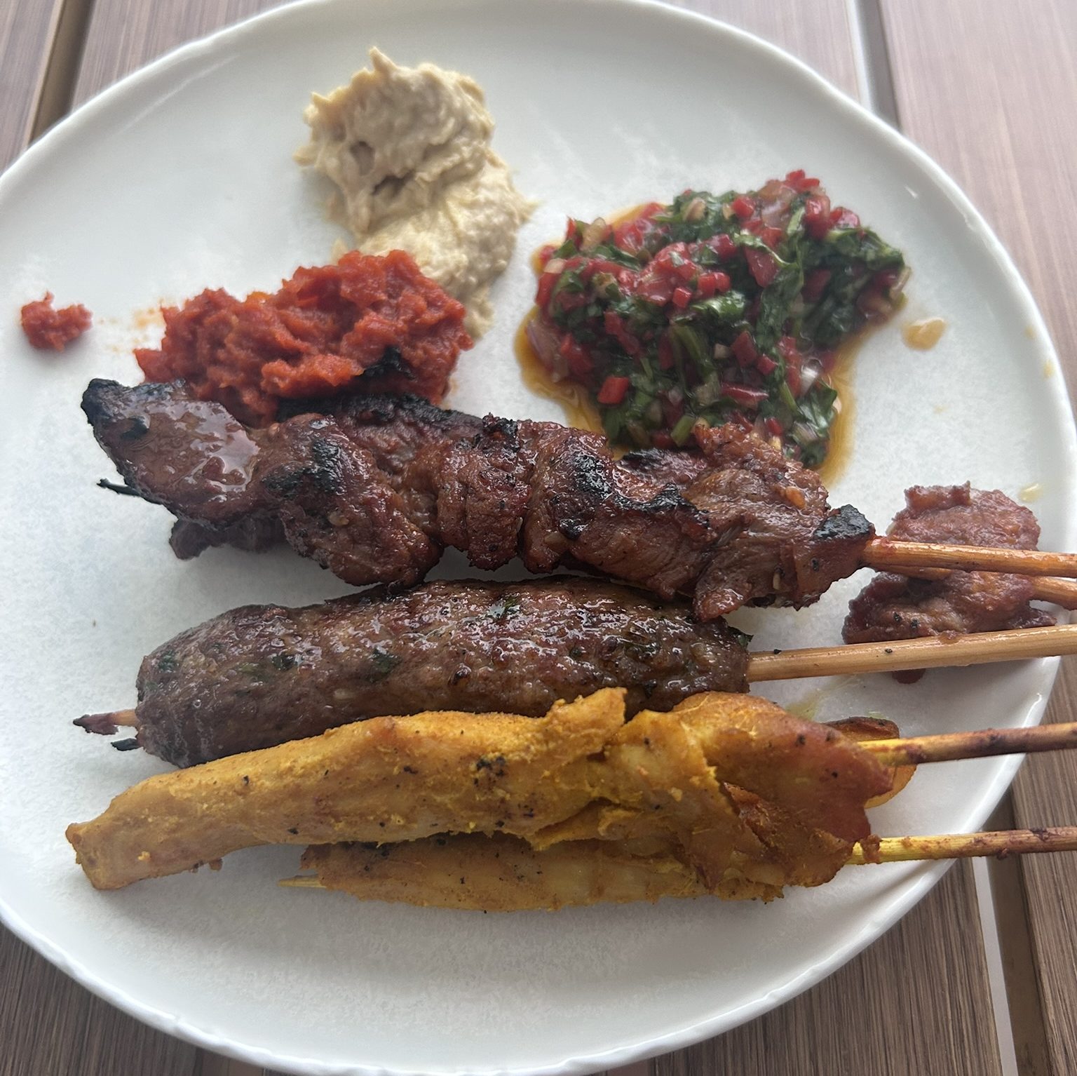 a plate full of beef and chicken skewers with sauces