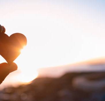 Hand holding up red heart to the sunset sky